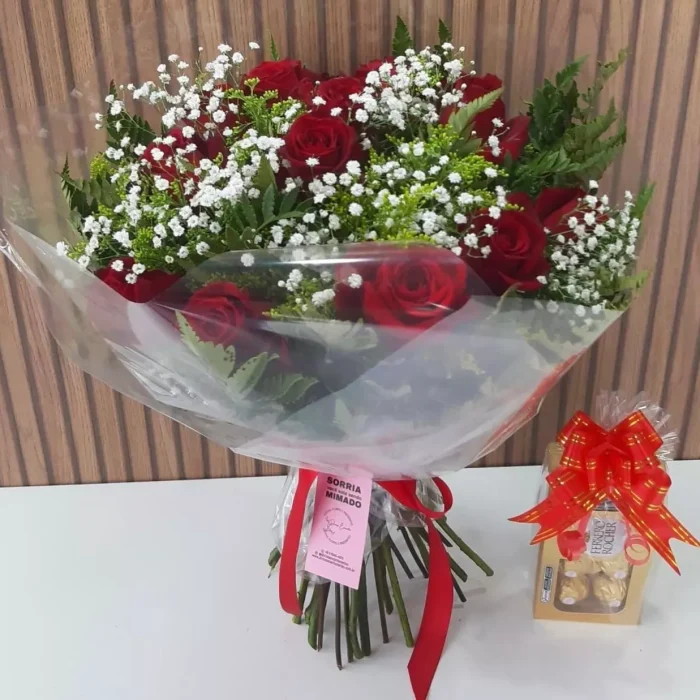 Buquê de rosas vermelhas com gypsophila e folhagens, embalado em papel transparente com laço vermelho, acompanhado de caixa de bombons Ferrero Rocher.