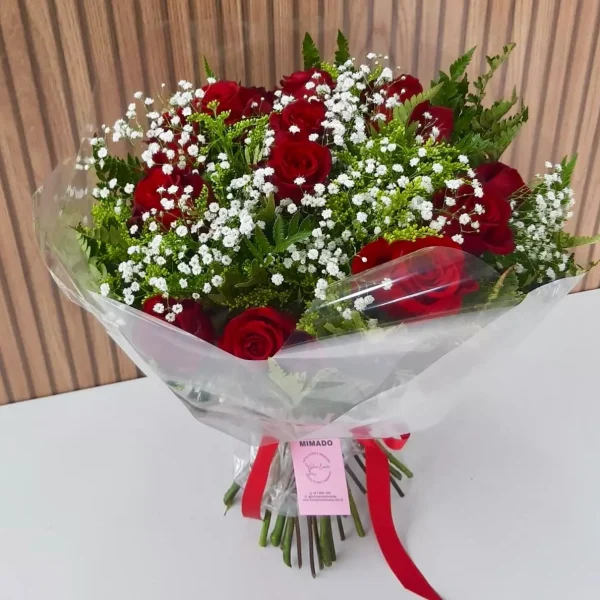 Buquê de rosas vermelhas com gypsophila e folhagens, embalado em papel transparente com laço vermelho, acompanhado de caixa de bombons Ferrero Rocher.