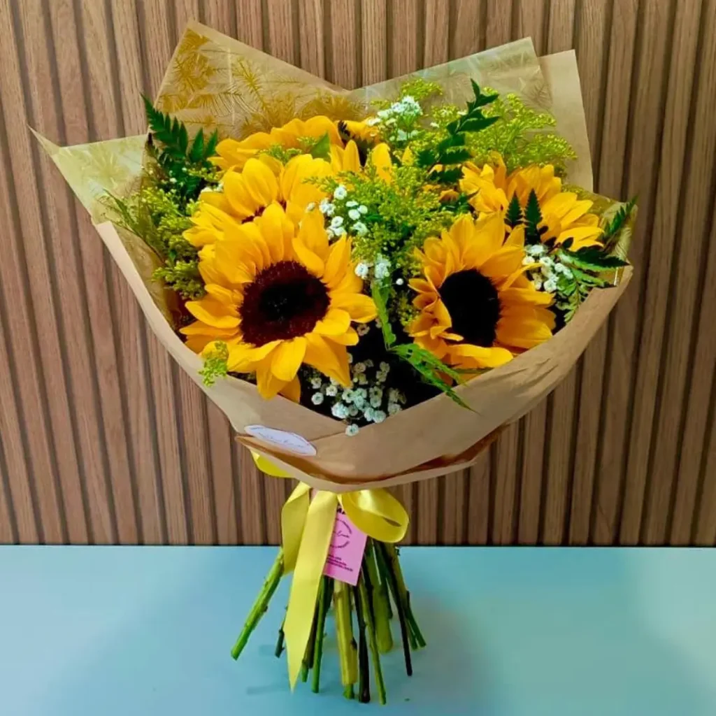 Buquê de girassóis com seis flores amarelas vibrantes, embalado em papel kraft e laço amarelo.