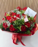 Buquê com 12 rosas vermelhas com gipsofila branca e folhagens verdes, embalado em papel vermelho com laço decorativo