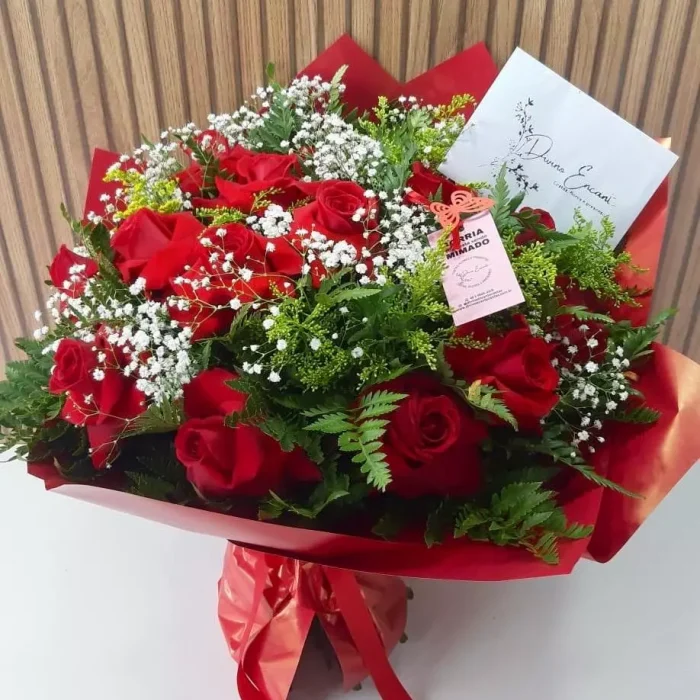 Buquê com 12 rosas vermelhas com gipsofila branca e folhagens verdes, embalado em papel vermelho com laço decorativo
