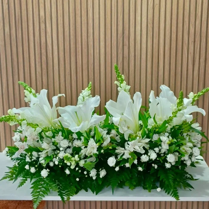 Arranjo de flores brancas com lírios, astromélias e folhagens verdes, ideal para homenagens e decorações elegantes.