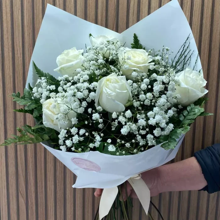 uquê de rosas brancas com mosquitinho e folhagens, embalado em papel branco e laço delicado