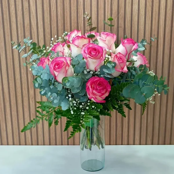 Arranjo de rosas cor-de-rosa e brancas em vaso de vidro transparente com folhagens e eucalipto.