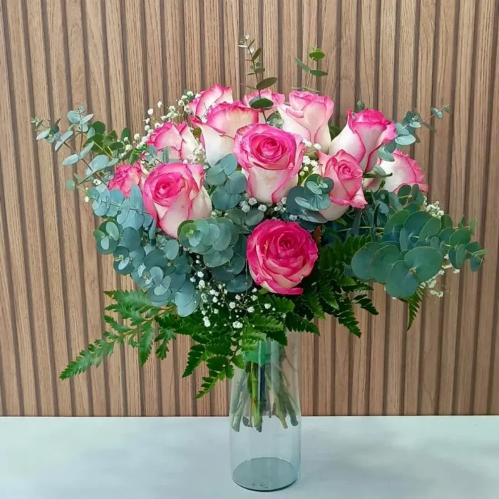 Arranjo de rosas cor-de-rosa e brancas em vaso de vidro transparente com folhagens e eucalipto.